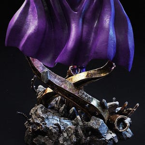 May include: A detailed statue featuring a flowing purple cape over a metallic structure. The statue rests on a rocky base with intricate details. The metallic elements have a weathered, aged appearance, with hints of gold and silver.