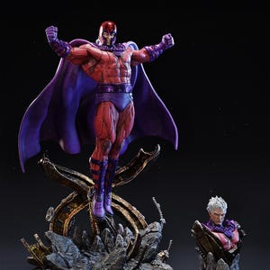 May include: A detailed statue of a superhero in a dynamic pose, wearing a red and purple costume with a flowing cape. The figure is posed with arms raised, atop a metallic, rocky base. A smaller bust of the character is also visible.