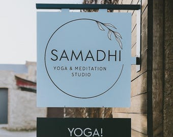May include: Sign for a yoga and meditation studio. The top sign is light blue with the word "SAMADHI" in black, a circular design, and the words "YOGA & MEDITATION STUDIO". The bottom sign is black and reads "YOGA!".