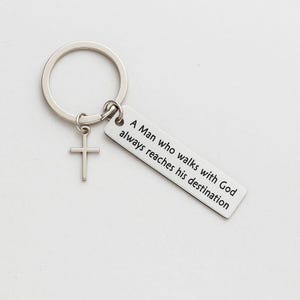 May include: Silver-coloured keyring with a cross charm and a rectangular tag. The tag is inscribed with the words: "A Man who walks with God always reaches his destination."