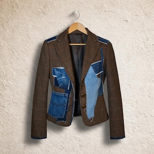 May include: A brown blazer with denim patchwork detailing. The jacket has a classic notched lapel, a three-button closure, and denim patches on the front and shoulders. It hangs on a wooden hanger against a textured wall.