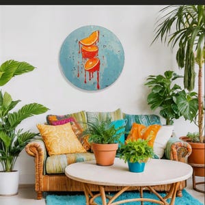 May include: A living room scene with a round painting of orange slices dripping red paint. A wicker sofa with colorful pillows sits in front of the painting. Potted plants and a round coffee table complete the decor.