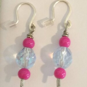 May include: A pair of dangle earrings with silver-tone hooks. Each earring features a bright pink bead, a faceted iridescent bead, and another pink bead. The earrings are designed for pierced ears.