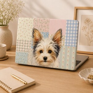 May include: A laptop skin featuring a portrait of a Yorkshire Terrier dog centered against a background of various pastel-colored patchwork patterns, including floral prints, pink stripes, and a light blue gingham check design.