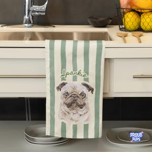 May include: A kitchen towel with vertical green stripes and a watercolor image of a pug dog. The word "Sparkie" is written in cursive above the dog. The towel is hanging in a kitchen.