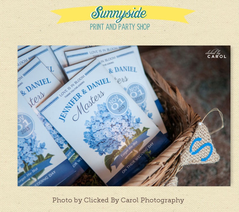 May include: A basket filled with small blue and white paper packets with the text "Jennifer & Daniel Masters" and "Love is in Bloom" printed on them. The packets are decorated with a blue hydrangea flower illustration and a blue circle with the date "Nov 01 2013".
