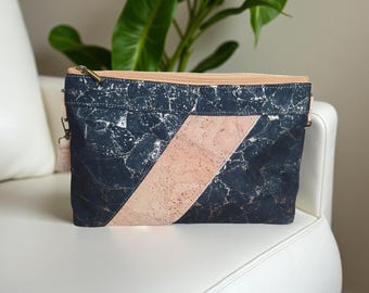 Pode incluir: Uma bolsa transversal azul marinho e rosa com um padrão de mármore e uma faixa diagonal rosa. A bolsa tem um zíper dourado e uma alça rosa claro. A bolsa está em uma superfície branca.