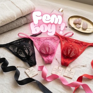 Może przedstawiać: Trzy stringi z czarnej, różowej i czerwonej koronki, każdy z zaokrągloną przednią kieszonką. Tekst "Fem boy!" jest wyświetlany białymi literami z różową poświatą. Każdy element zawiera małą kwadratową metkę z napisem "Handmade Lace."