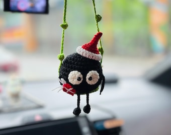 May include: A handmade black crochet character with large white eyes, wearing a red and white Santa hat, and holding a small red gift. The character is suspended by green vines and is designed as a car accessory.