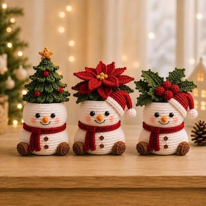 May include: Three crocheted snowmen figures with white bodies, red scarves, and brown feet. The first wears a green Christmas tree, the second a red poinsettia and Santa hat, and the third a green holly sprig with red berries and a Santa hat.