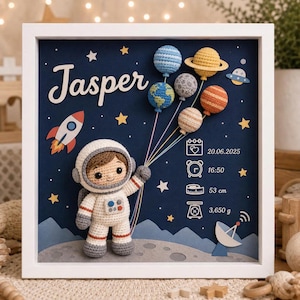 Può includere: Una cornice bianca con un astronauta all'uncinetto che tiene dei fili collegati a cinque pianeti all'uncinetto. Lo sfondo blu scuro mostra il nome Jasper, un razzo, stelle e i dati di nascita: 20.06.2025, 16:50, 53 cm e 3.650 g.