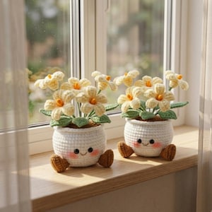 Puede incluir: Dos macetas de flores hechas a mano con caras sonrientes y pies marrones están sobre un alféizar de madera. Cada maceta contiene flores de ganchillo amarillas y naranjas con hojas verdes. Las macetas son blancas y tienen un aspecto texturizado.