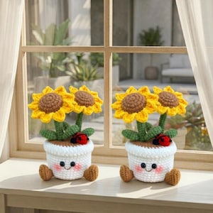 May include: Two crochet sunflower arrangements in white pots with smiling faces and brown feet. Each pot has two sunflowers with yellow petals and brown centres, green leaves, and a red ladybird. The arrangement sits on a wooden windowsill.