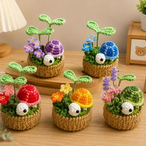 May include: Five crocheted turtle figurines in tan woven bases, each featuring a colorful patterned shell, a white head with black eyes, and a green sprout. The shells are purple, blue, red, orange, and green, accented with small crocheted flowers.