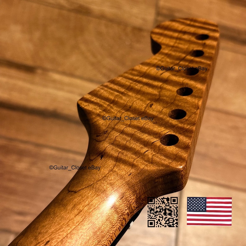 Op de afbeelding: Een gitaarkop gemaakt van lichtbruin hout met een opvallend tijgergestreept vlam-esdoornnerfpatroon. De kop heeft zes ronde gaten voor stemmechanieken op een rij en bevat een QR-code en een kleine Amerikaanse vlag-icoon.