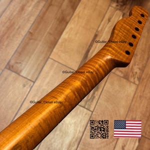 May include: A close-up of a guitar neck with a flamed maple finish. The neck is a warm amber color with visible wood grain. The headstock has tuning peg holes. The image includes the text "Guitar Closet eBay" and a QR code.