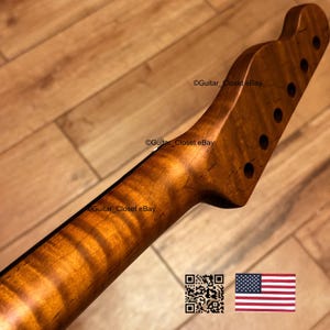 May include: A guitar neck with a flamed maple finish. The neck has a natural wood grain pattern with a warm, amber hue. The headstock features six tuning peg holes. The text "Guitar Closet eBay" is visible.