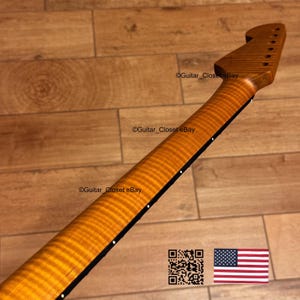 May include: A close-up of a guitar neck with a flamed maple finish. The neck is a warm, golden brown color with a striped pattern. The fretboard is black with white dot inlays. The headstock has tuning peg holes. The text "Guitar_Closet eBay" is visible.