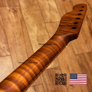 May include: A close-up of a guitar neck made of figured wood, showcasing a rich, warm brown color with intricate grain patterns. The neck has pre-drilled holes for tuning pegs and a smooth, curved profile. The text "Guitar Closet eBay" is visible.