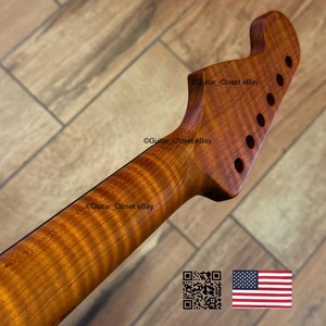 May include: A close-up of a wooden guitar neck and headstock with a flamed maple grain pattern. The headstock has six tuning peg holes. The wood has a warm, amber color. The image includes a QR code and an American flag.