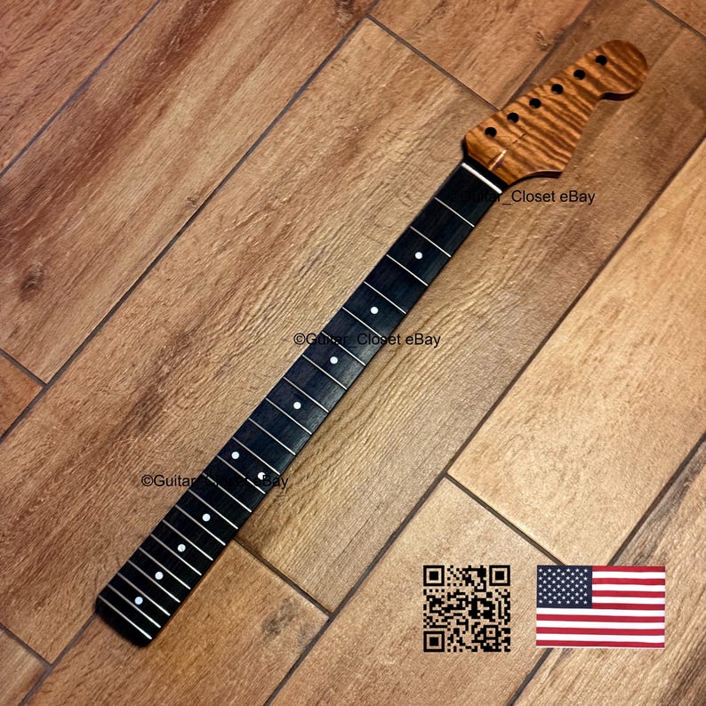 Puede incluir: Un m&aacute;stil de guitarra con un diapas&oacute;n de madera oscura con incrustaciones de puntos blancos y una pala de madera marr&oacute;n claro con vetas de tigre. La pala tiene seis orificios para clavijas en fila. Un c&oacute;digo QR y una bandera de EE. UU. son visibles.