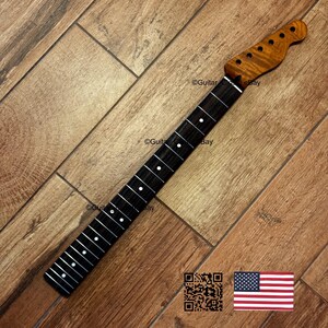 Puede incluir: M&aacute;stil de guitarra con diapas&oacute;n oscuro e incrustaciones de puntos blancos. El clavijero es de madera m&aacute;s clara con acabado natural. El m&aacute;stil est&aacute; inclinado sobre una superficie de madera. La bandera americana est&aacute; en la esquina inferior derecha.