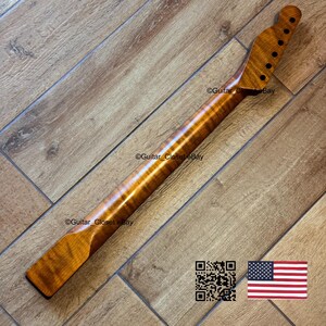 May include: A guitar neck made of figured maple wood, featuring a natural finish. The neck has a headstock with tuning peg holes and a fretboard area. The wood grain is visible. The image includes a QR code and an American flag.