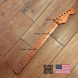 Pode incluir: Um bra&ccedil;o de guitarra novo, inacabado, feito de madeira clara. O bra&ccedil;o tem um cabe&ccedil;ote com orif&iacute;cios pr&eacute;-perfurados para as cravelhas e uma escala com marcadores de traste embutidos. A imagem inclui um c&oacute;digo QR e uma pequena bandeira americana.