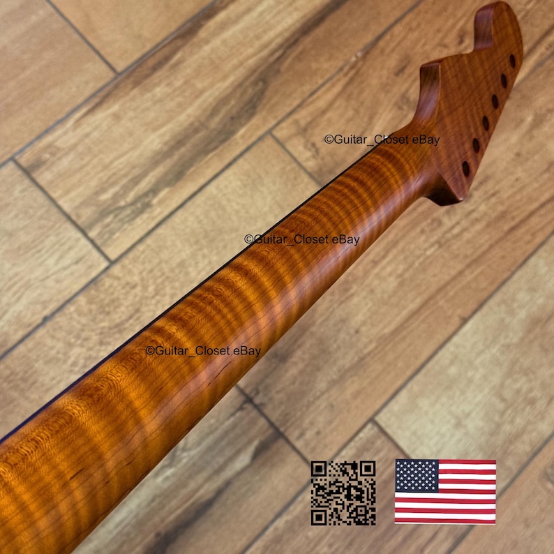 May include: A close-up of a guitar neck made of figured maple wood. The neck has a natural wood finish with a wavy grain pattern. The headstock has pre-drilled holes for tuning pegs. The image includes a QR code and the American flag.