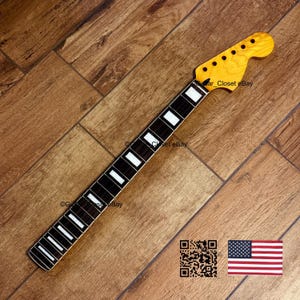 K&ouml;nnte beinhalten: Ein Gitarrenhals mit einer hellen Kopfplatte und einem dunklen Griffbrett mit wei&szlig;en Einlagen. Der Hals ist vor einem Holzgrund platziert. Das Bild enth&auml;lt einen QR-Code und eine kleine amerikanische Flagge.