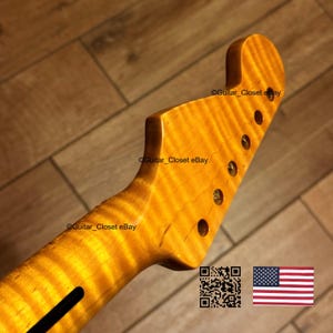 May include: A close-up of a guitar neck and headstock with a flamed maple finish. The wood has a warm, golden hue with visible grain patterns. The headstock features six tuning peg holes. The text "Guitar_Closet eBay" is visible.