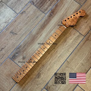 May include: A light brown guitar neck with a headstock featuring tuning peg holes. The neck has frets and dot inlays. The image includes a QR code and a small American flag.