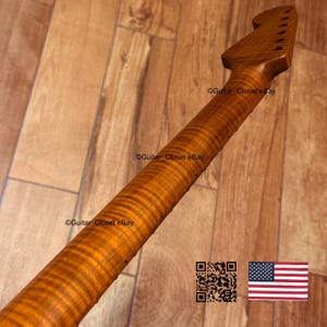 May include: A close-up of a guitar neck made of figured maple wood. The wood has a warm, amber hue with prominent grain patterns. The headstock features tuning peg holes. The image includes a QR code and a US flag.