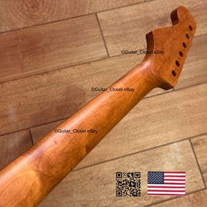 Pode incluir: Bra&ccedil;o de guitarra feito de madeira castanha clara, com um headstock com orif&iacute;cios para as cravelhas. O bra&ccedil;o tem um acabamento liso e polido. A imagem inclui um c&oacute;digo QR e a bandeira americana.