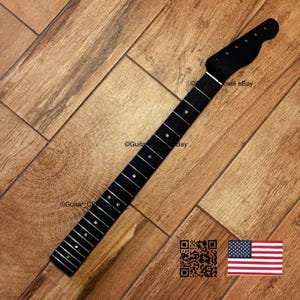 May include: A black guitar neck with silver frets and dot inlays. The headstock is also black. The neck is angled on a wooden surface. A QR code and American flag are in the lower right corner.