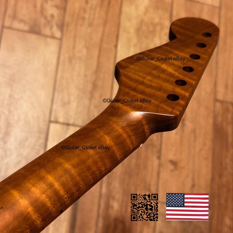 Op de afbeelding: Een close-up van een gitaarhals van gevlamd hout. De hals heeft een warme bruine kleur met een glanzende afwerking. De kop heeft zes gaten voor de stemknoppen. De tekst "Guitar Closet eBay" is zichtbaar.