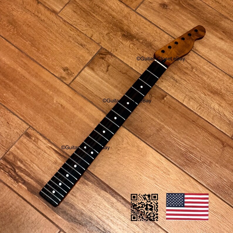 May include: A guitar neck with a dark fretboard and white fret markers. The headstock is a lighter wood color with tuning peg holes. The neck is angled on a wooden surface. The image includes a QR code and an American flag.