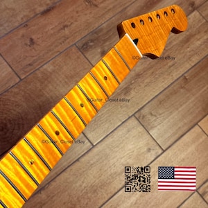 May include: A maple guitar neck with a flamed finish. The neck has a headstock with tuning peg holes and a fretboard with inlaid position markers. The wood grain is visible, and the neck is a warm amber color.