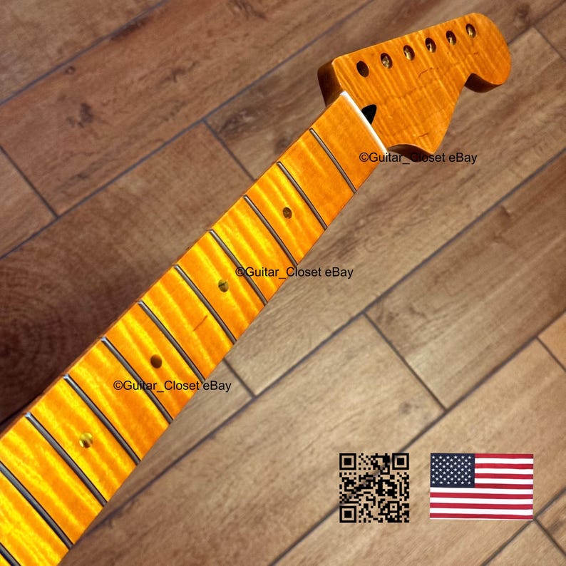 May include: A maple guitar neck with a flamed finish. The neck has a headstock with tuning peg holes and a fretboard with inlaid position markers. The wood grain is visible, and the neck is a warm amber color.