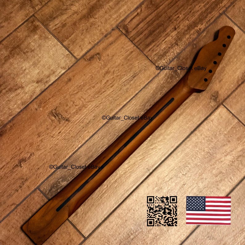 Op de afbeelding: Een houten gitaarhals met een kop met zes gaten voor de stemknoppen. De hals heeft een donkere streep in het midden en ligt op een houten vloer. De afbeelding bevat een QR-code en een Amerikaanse vlag.