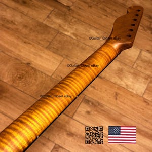 May include: A close-up of a guitar neck with a flamed maple finish. The neck is a warm amber color with a wavy grain pattern. The headstock has tuning peg holes. The text "Guitar_Closet eBay" is visible. An American flag is in the bottom right corner.