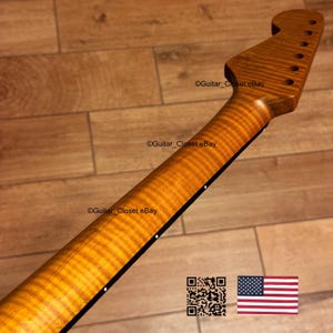 May include: A guitar neck with a flamed maple finish. The neck has a natural wood color with a prominent grain pattern. The headstock features tuning peg holes. The image includes a QR code and a small American flag.