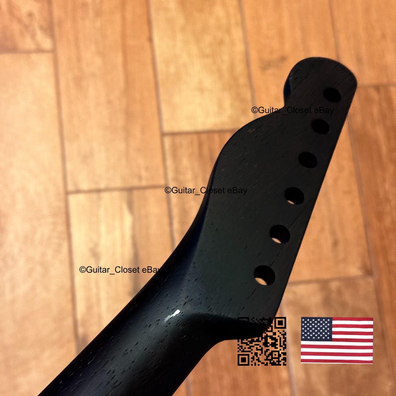 May include: A black guitar neck with six tuning peg holes. The headstock has a rounded shape. The neck is angled and has a smooth, dark finish. The image includes a QR code and a small American flag.
