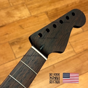 Peut inclure: Un manche de guitare brun fonc&eacute; avec une t&ecirc;te comportant des trous pour les chevilles d'accord. La touche a des frettes argent&eacute;es et un bord blanc. L'image comprend un code QR et le drapeau am&eacute;ricain.
