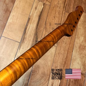 May include: A guitar neck with a flamed maple finish. The neck is a warm amber color with dark brown grain patterns. The headstock has six tuning peg holes. The text "Guitar_Closet eBay" is visible.