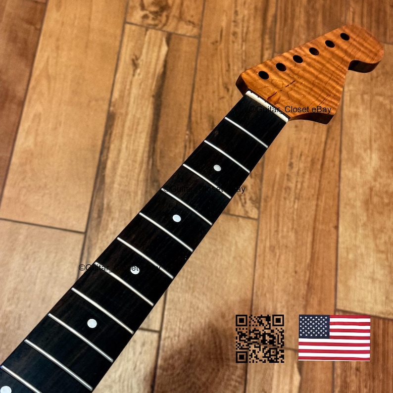 Puede incluir: Un m&aacute;stil de guitarra con diapas&oacute;n de madera oscura, marcadores de posici&oacute;n circulares blancos y trastes plateados. El clavijero es de madera marr&oacute;n clara con un veteado flameado y seis orificios para las clavijas de afinaci&oacute;n.