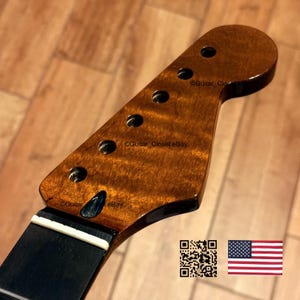 May include: A close-up of a guitar headstock with a dark, glossy finish. The wood grain is visible, with a rich, brown color. There are six tuning peg holes. The neck is black with a white strip. The text "Guitar Closet eBay" is visible.