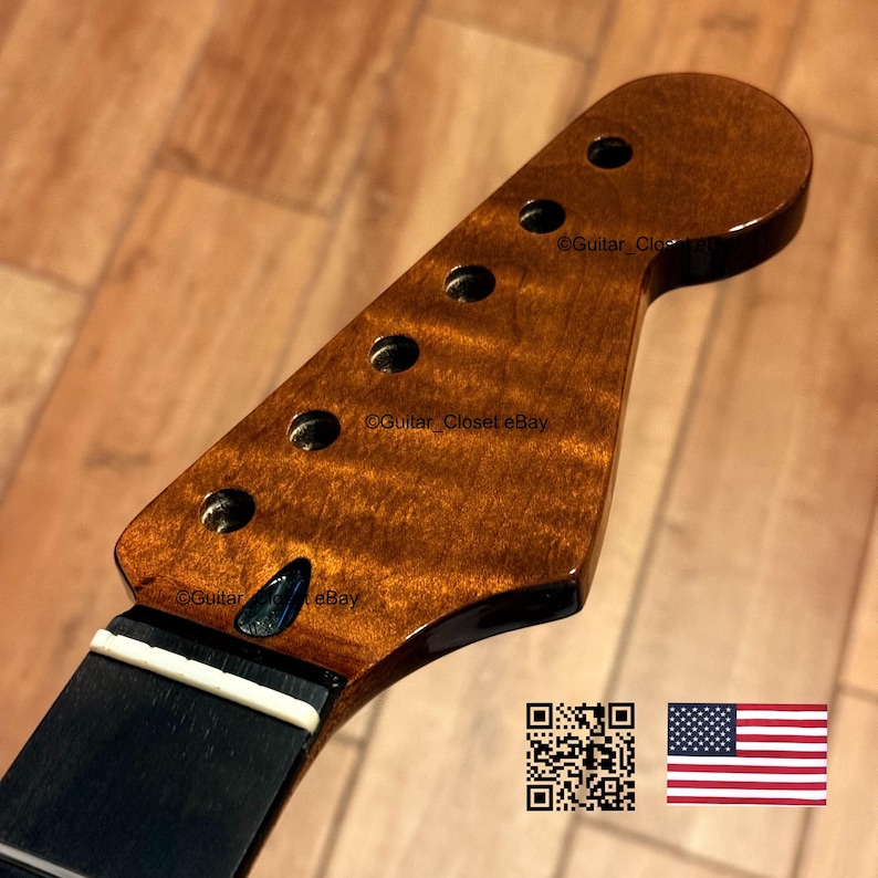 May include: A close-up of a guitar headstock with a dark, glossy finish. The wood grain is visible, with a rich, brown color. There are six tuning peg holes. The neck is black with a white strip. The text "Guitar Closet eBay" is visible.
