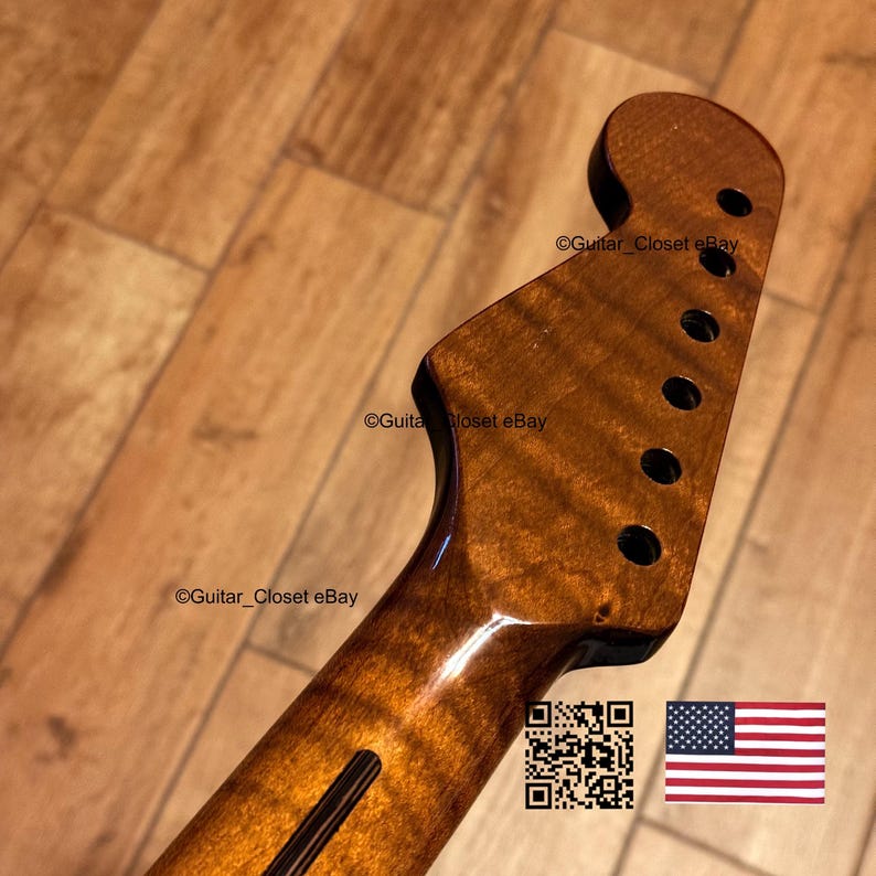 May include: A guitar neck with a flamed maple finish. The headstock has six tuning peg holes. The neck is a warm brown color with a glossy finish. The image includes a QR code and the American flag.