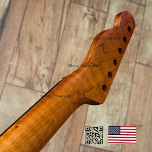 以下が含まれることがあります： 自然な仕上がりの木製ギターネック。ヘッドストックには6つのペグ穴があります。ネックは明るい茶色で、より濃い木目模様があります。画像にはQRコードとアメリカ国旗が含まれています。